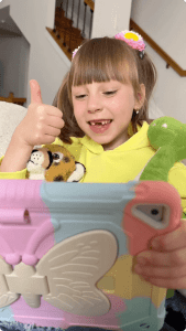 A young girl gives a thumbs up while holding a tablet in a colorful case, engaging in digital learning.