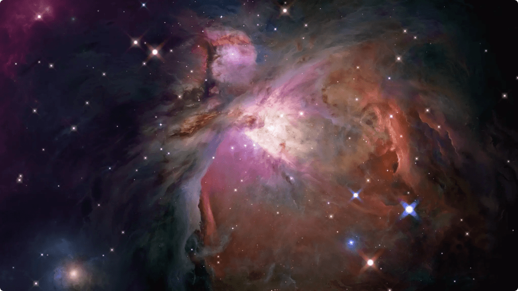A dazzling image of the Orion Nebula, a diffuse nebula with bright pink, purple, and red gases, and many stars.